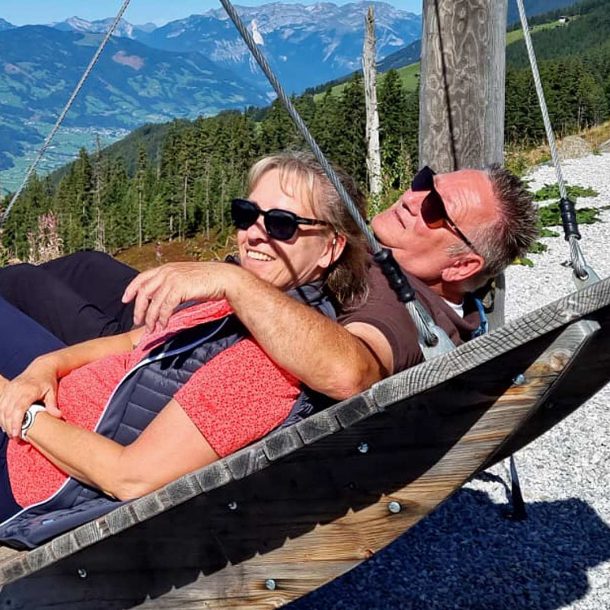 Die Gastgeber des Ferienhauses Casa La Vie stehen im Mittelpunkt des Bildes. Sie wirken herzlich und offen – ein echtes Herz für Gäste. Ihre entspannte Haltung und ihre freundlichen Gesichter zeigen gelebte Gastfreundschaft. Sie liegen gemeinsam auf einer Schaukel. Ihr Blick geht über ein Tal und auf Berge in der Ferne. Sie lachen und zeigen Humor und Entspannung. Ihre Präsenz vermittelt Vertrauen und lässt Gäste sich willkommen fühlen.